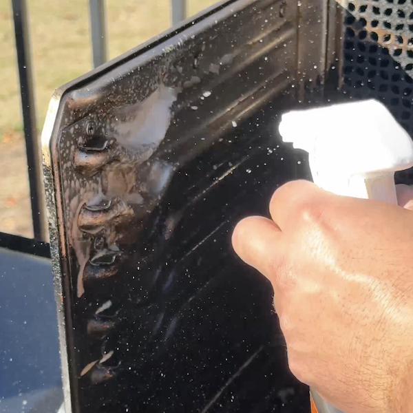 applying cleaning spray to grill